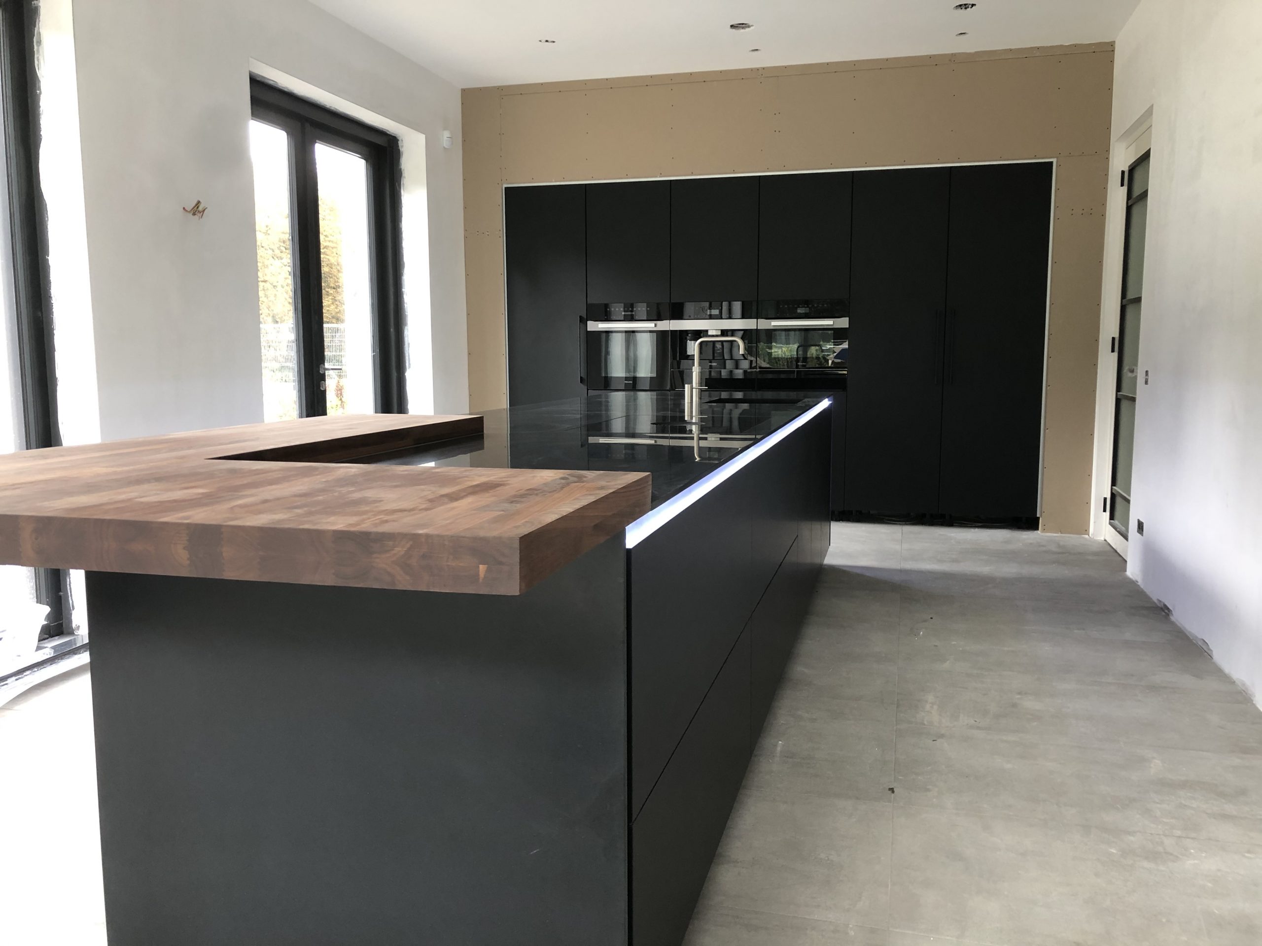 Gemonteerde zwarte keuken met houten barblad en ingebouwde apparatuur